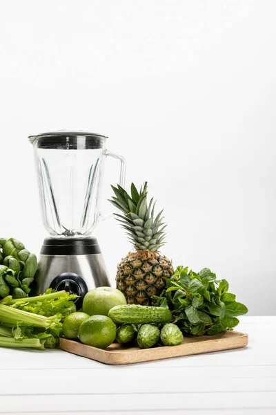 Grüne frische Spinatblätter in der Nähe von Bio-Sellerie, Gurken, Früchten und Mixer auf weiß — Stockfoto