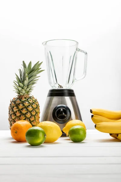 Blender near ripe pineapple, lemons, orange, yellow bananas and green limes on white — Stock Photo