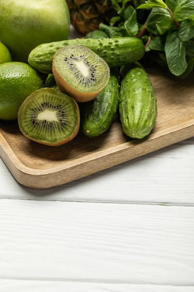Halves of tasty ripe kiwi fruit near cucumbers on wooden cutting board — Stock Photo