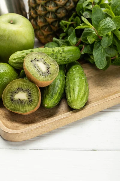 Halves of ripe kiwi fruit near cucumbers, apple and pineapple on wooden chopping board — Stock Photo