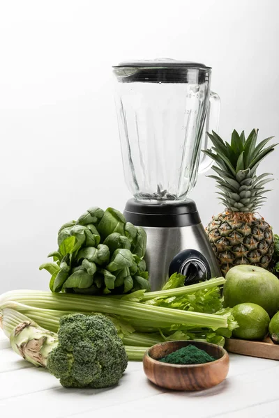 Licuadora cerca de verduras frescas, verdes y frutas orgánicas en blanco - foto de stock