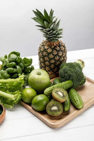 Tasty fresh pineapple, apple and limes near organic and raw vegetables on grey — Stock Photo