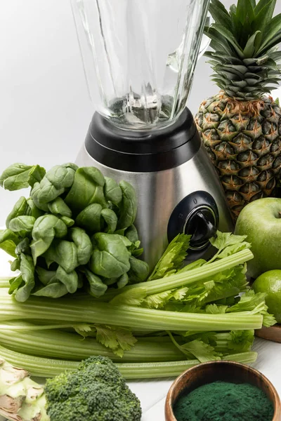 Licuadora cerca de frutas frescas y verduras verdes orgánicas en blanco - foto de stock