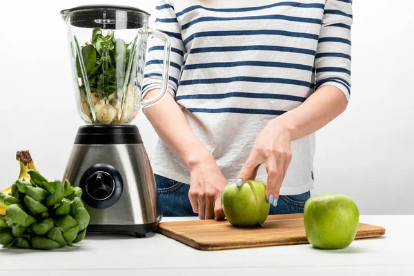 Vista ritagliata di donna taglio mela verde vicino frullatore e banane su bianco — Foto stock