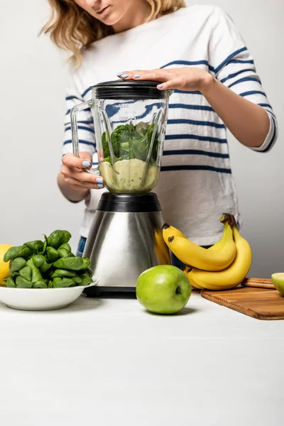 Vue recadrée de la femme en utilisant un mélangeur près de fruits biologiques sur blanc — Photo de stock