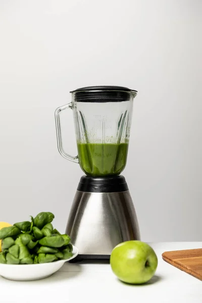 Grüner leckerer Apfel in der Nähe von Spinatblättern und Mixer auf grau — Stockfoto