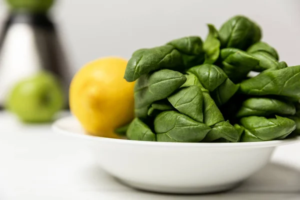Selektiver Fokus grüner frischer Spinatblätter in der Nähe gelber Zitrone auf weißer — Stockfoto