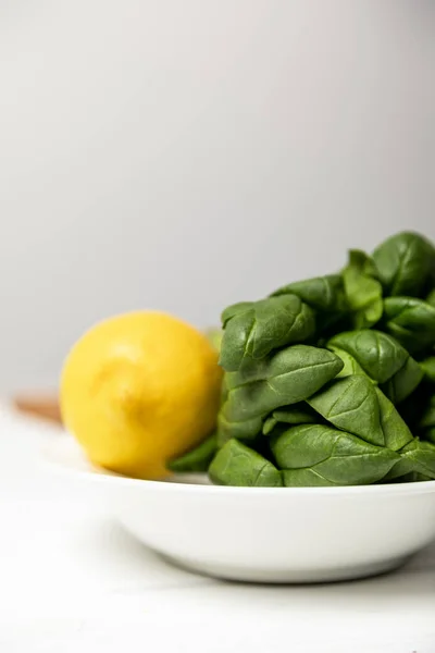 Selective focus of fresh spinach leaves near yellow ripe lemon on grey — Stock Photo