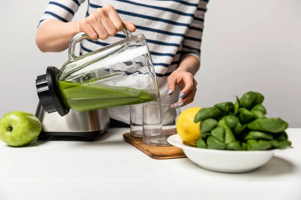 Vista ritagliata della donna versando gustoso frullato verde in vetro vicino mela su grigio — Foto stock