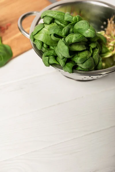 Frische grüne und organische Spinatblätter im Sieb auf weißer Oberfläche — Stockfoto