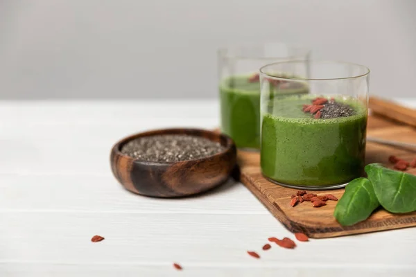 Gustoso frullato verde in bicchieri con semi di chia e bacche di goji su grigio — Foto stock