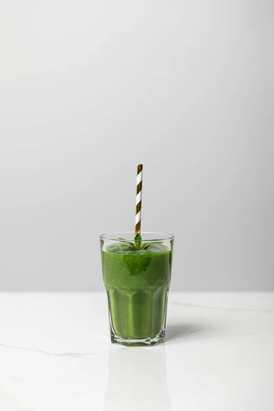 Вкусный, зеленый и органический смузи в стакане с соломой на сером — стоковое фото