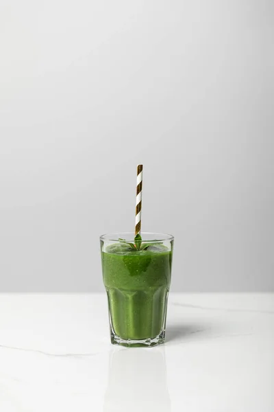 Batido sabroso, verde y orgánico en vidrio con paja sobre gris - foto de stock