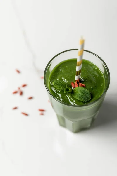 Selektiver Fokus von grünem Smoothie mit Goji-Beeren und Minze im Glas mit Stroh auf Weiß — Stockfoto