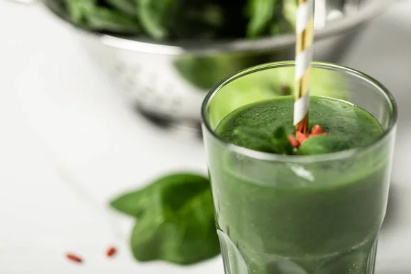 Fuoco selettivo di frullato verde saporito in vetro con paglia vicino a foglie di spinaci fresche su bianco — Foto stock
