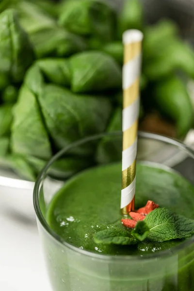 Foyer sélectif de smoothie en verre avec de la paille près des feuilles d'épinards frais sur blanc — Photo de stock