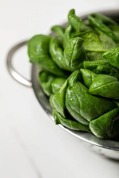 Selective focus of green fresh and organic spinach leaves in colander on white — Stock Photo