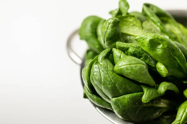 Selective focus of green and fresh spinach leaves in colander on white — Stock Photo