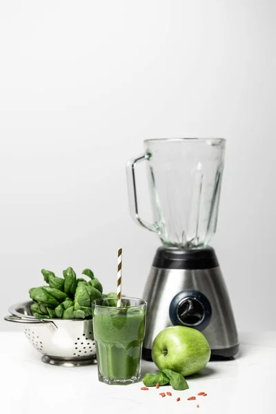Smoothie savoureux en verre avec de la paille près des feuilles d'épinards frais, pomme et mélangeur sur blanc — Photo de stock