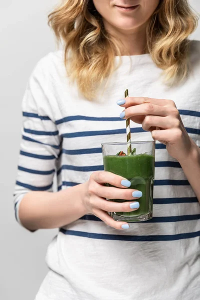 Cropped view of happy woman holding straw and glass with tasty green smoothie on white — Stock Photo