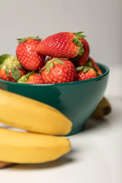 Selective focus of sweet strawberries in bowl near yellow bananas on grey — Stock Photo