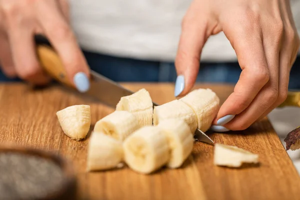 Vista recortada de mujer cortando plátanos maduros y dulces en la tabla de cortar - foto de stock
