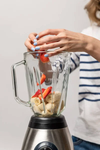 Vista ritagliata della donna che mette le fragole rosse nel frullatore con le banane sul bianco — Foto stock