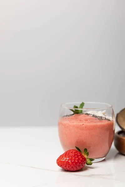 Leckerer Smoothie im Glas neben leckerer reifer Erdbeere auf Grau — Stockfoto
