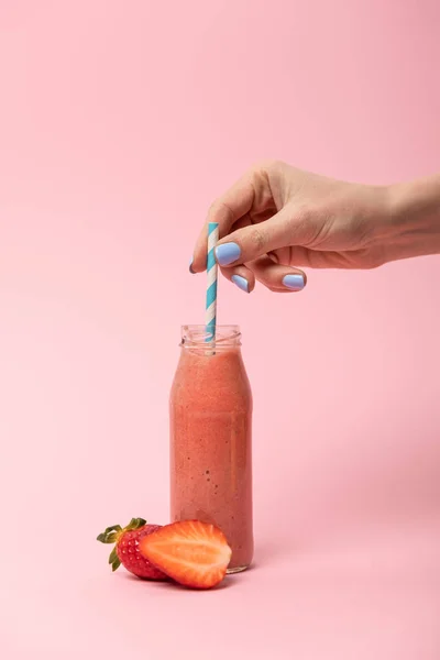 Abgeschnittene Ansicht einer Frau mit Strohhalm in Glasflasche mit leckerem Smoothie in der Nähe reifer Erdbeeren auf rosa — Stockfoto