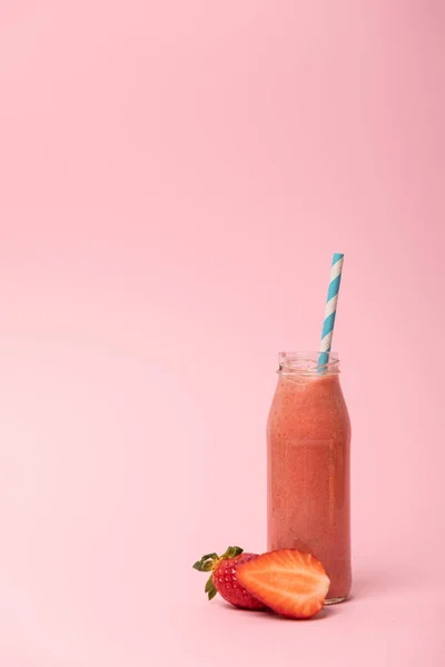 Сладкий и вкусный смузи в стеклянной бутылке с соломой возле клубники на розовом — стоковое фото