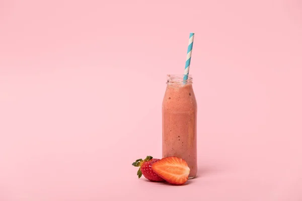 Сладкий и вкусный смузи в стеклянной бутылке с соломой возле красной клубники на розовом — стоковое фото