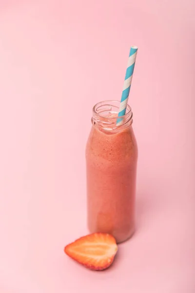 Smoothie doce e saboroso em garrafa de vidro com palha perto de morangos maduros isolados em rosa — Fotografia de Stock