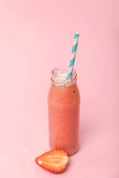 Süßer und schmackhafter Smoothie in Glasflasche mit Stroh in der Nähe von roten Erdbeeren auf rosa — Stockfoto