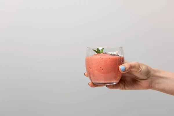 Vista cortada de mulher segurando vidro com saboroso smoothie rosa no cinza — Fotografia de Stock