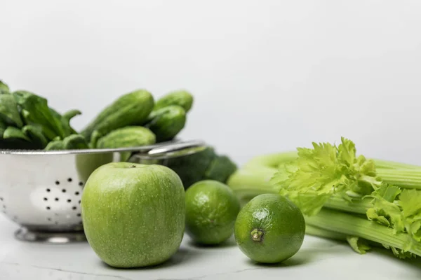 Selective focus of sweet apple near green limes and cucumbers on white — Stock Photo