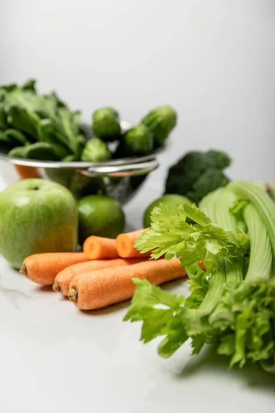 Selektiver Fokus von Sellerie in der Nähe von Karotten, reifen Äpfeln und grünem Gemüse auf grau — Stockfoto