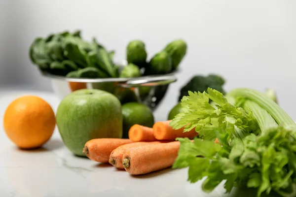 Foco selectivo de apio cerca de zanahorias dulces, manzana madura y verduras verdes en gris - foto de stock