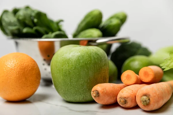 Selective focus of green apple, orange and carrots near green cucumbers on white — Stock Photo
