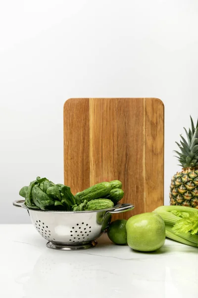 Fruits mûrs près de légumes verts frais et planche à découper en bois sur blanc — Photo de stock