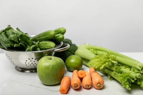 Zanahorias dulces cerca de la manzana madura y verduras verdes en gris - foto de stock