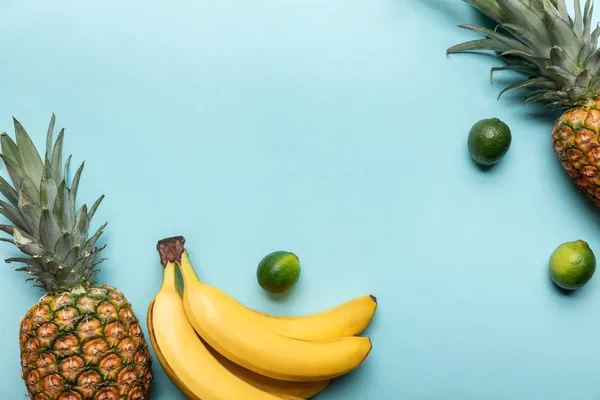 Vista dall'alto di interi ananas maturi, banane e lime su sfondo blu con spazio per copiare — Foto stock