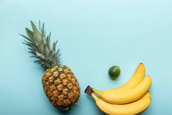 Vista dall'alto di tutto l'ananas maturo, banane e lime su sfondo blu con spazio copia — Foto stock