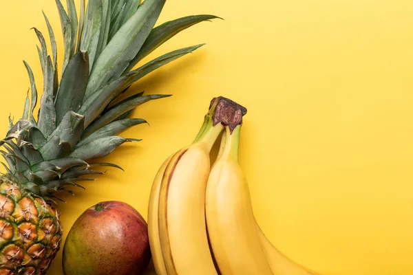 Top view of whole ripe bananas, pineapple and mango on yellow background — Stock Photo