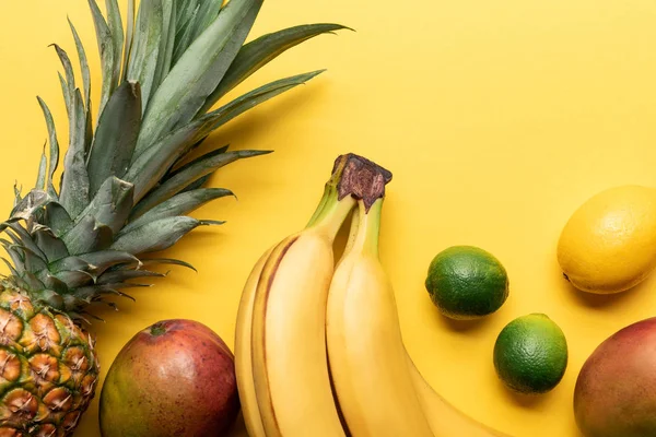 Vista superior de bananas maduras inteiras, abacaxi, frutas cítricas e manga no fundo amarelo com espaço de cópia — Fotografia de Stock