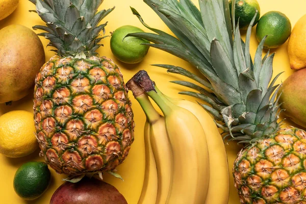 Vista superior de plátanos maduros enteros, piña, cítricos y mango sobre fondo amarillo - foto de stock