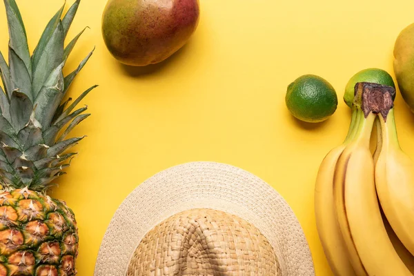 Top view of straw hat near pineapple, bananas, limes and mango on yellow background — Stock Photo