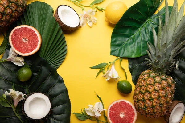 Vue de dessus des fruits tropicaux biologiques mûrs sur fond jaune avec des feuilles vertes et des fleurs d'Alstroemeria — Photo de stock