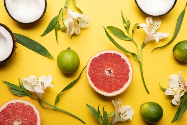 Top view of ripe organic tropical fruits on yellow background with Alstroemeria flowers — Stock Photo