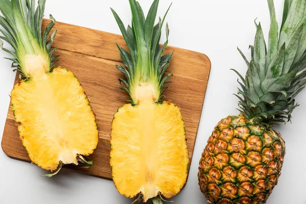 Vista superior de abacaxi amarelo maduro corte na tábua de corte de madeira perto de frutas inteiras no fundo branco — Fotografia de Stock