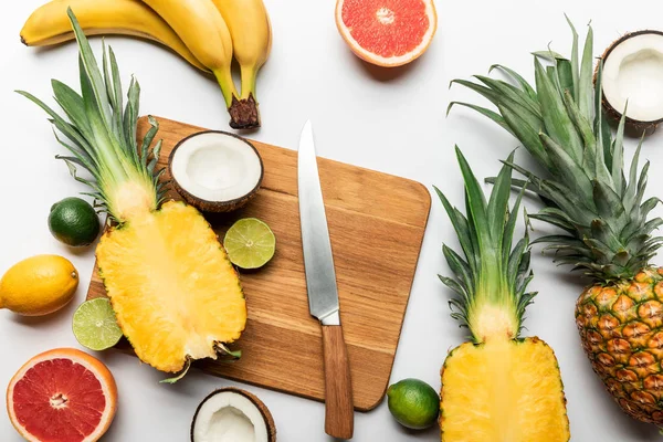 Vue du dessus des fruits tropicaux coupés et entiers sur planche à découper en bois près du couteau sur fond blanc — Photo de stock